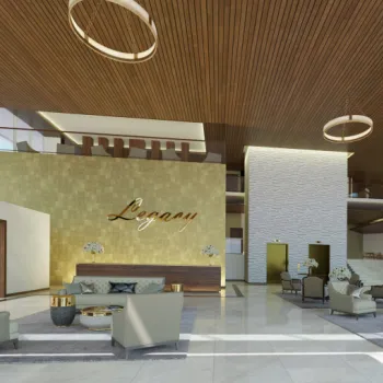 Modern hotel lobby with high ceilings, gold accents, large windows, seating areas, and the word "Legacy" displayed on a gold wall behind the reception desk.