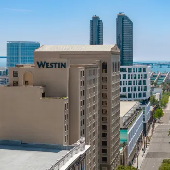 Aerial view of downtown city buildings with the Westin hotel in the foreground, two tall towers, and a bridge visible in the background on a clear day.