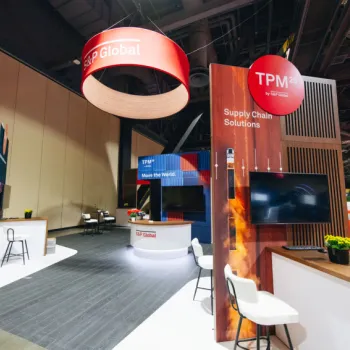 Trade show booth for TPM23 by S&P Global, featuring seating areas, branded displays, a TV screen, and overhead signage in a large convention hall.