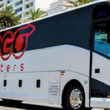 A white and black charter bus with "GOGO Charters" branding is parked on a city street lined with palm trees and modern buildings.