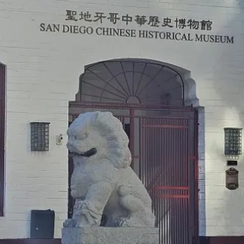 Entrance of the San Diego Chinese Historical Museum featuring a stone lion statue and posters in the windows.