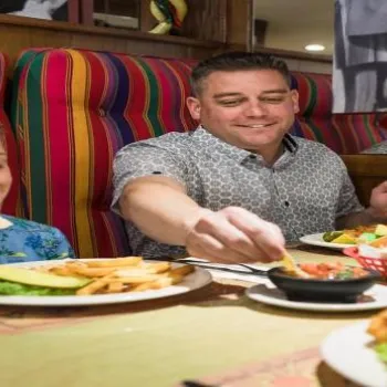 A man and a boy are sitting in a restaurant booth, eating a meal with sandwiches, fries, and drinks on the table.