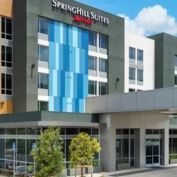 Modern SpringHill Suites by Marriott hotel exterior with large windows, covered entrance, and clear blue sky in the background.