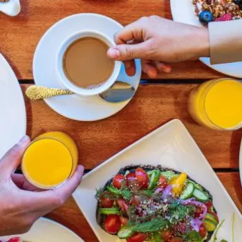 People having breakfast with pancakes, waffles, toast with avocado, orange juice, and coffee on a wooden table.