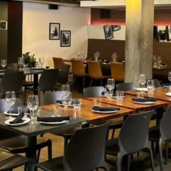 Modern restaurant dining area with neatly set tables, black chairs, wine glasses, and contemporary decor, including wall art and mirrors.