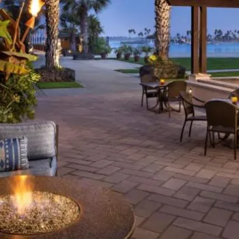 Outdoor patio area with seating around a fire pit, tables and chairs, overlooking a waterfront view at dusk.