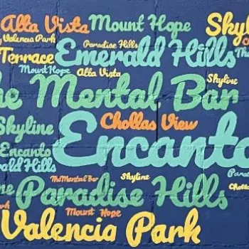 Word cloud mural on a blue brick wall featuring neighborhood names like Encanto, The Mental Bar, Valencia Park, Paradise Hills, and others in various colors and sizes.