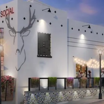 Punch Bowl Social building exterior at dusk, featuring string lights, outdoor seating, large deer head mural, and people on the patio.