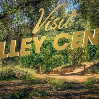 A sunlit forest path surrounded by green trees with the words "Visit Valley Center" in large gold letters across the image.