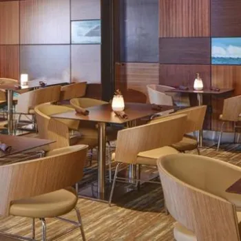 Modern restaurant with wooden tables and chairs, soft lighting, wall-mounted TVs displaying sports and nature scenes, and a contemporary decor featuring stone and wood paneling.