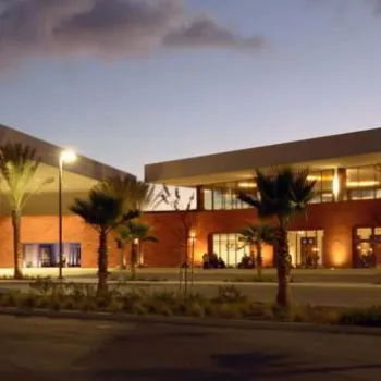 Exterior view of the CBX (Cross Border Xpress) terminal at dusk, with illuminated signage, palm trees, and parked cars in the foreground.