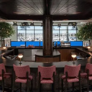 Circular bar with red chairs in a modern, spacious room with large windows overlooking a marina with boats.