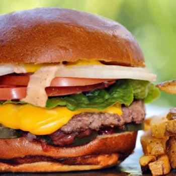 A cheeseburger with lettuce, tomato, onion, pickles, and sauce in a bun, served with a side of French fries.