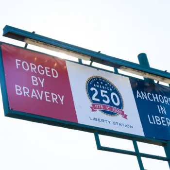 A billboard displays a banner reading "Forged by Bravery" and "Anchored in Liberty" with a "250 America 1776-2026" emblem in the center.