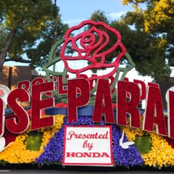 A Rose Parade float displays large red letters spelling "Rose Parade," a rose emblem, and a sign reading "Presented by Honda," surrounded by colorful flowers and trees.