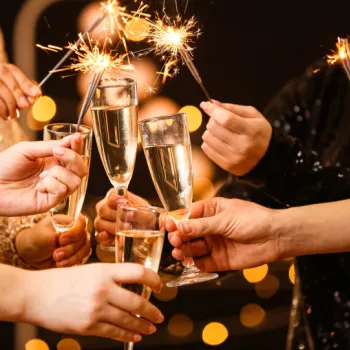 A group of people clinking champagne glasses and holding sparklers, with festive lights in the background.