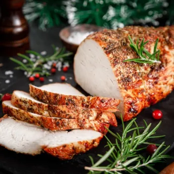 A roasted herb-crusted pork loin, partially sliced, is displayed on a slate board with fresh rosemary and cranberries.