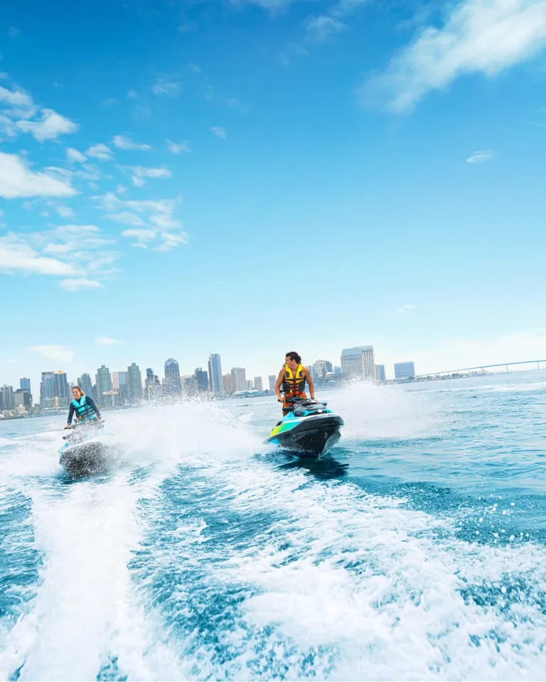 Two people, each on a jet ski in San Diego Bay racing on a clear blue day