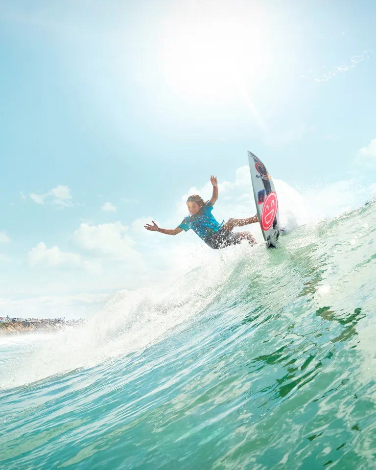 Young man catching an epic wave on a surfboard with a smile graphic in San Diego