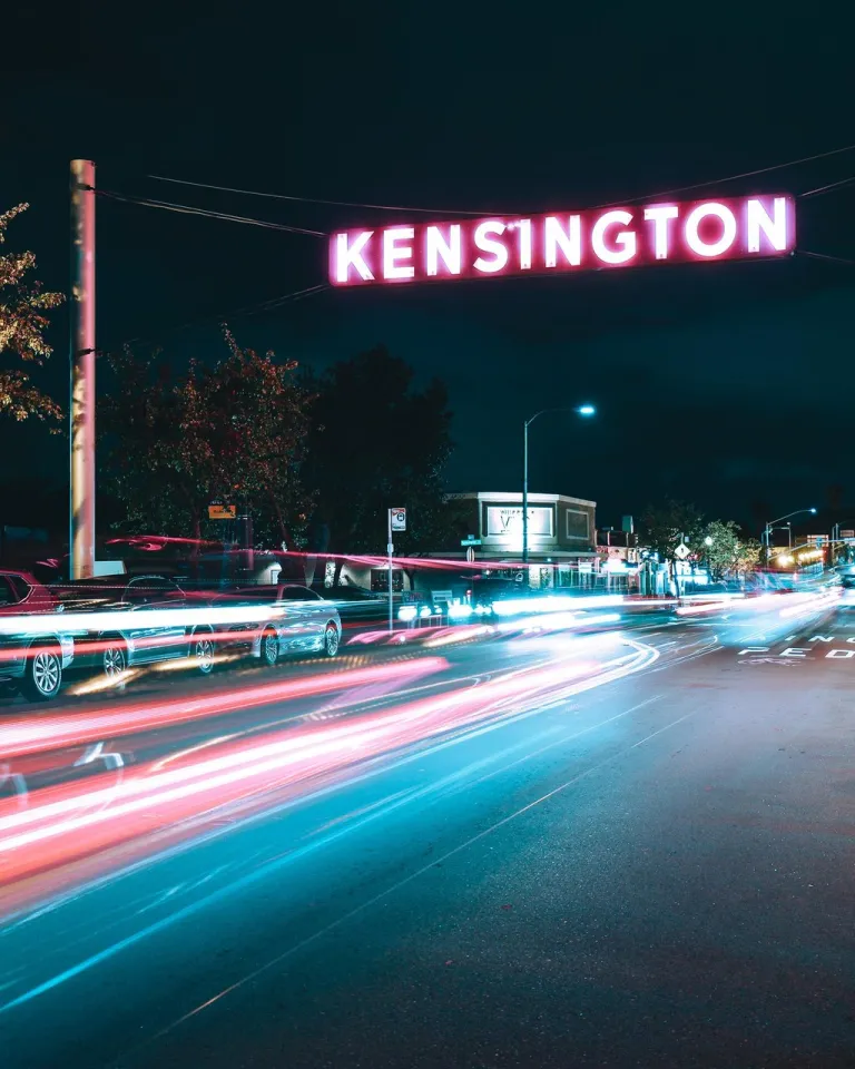 Kensington Neighborhood sign over a nighttime time-lapse of car lights streaks.