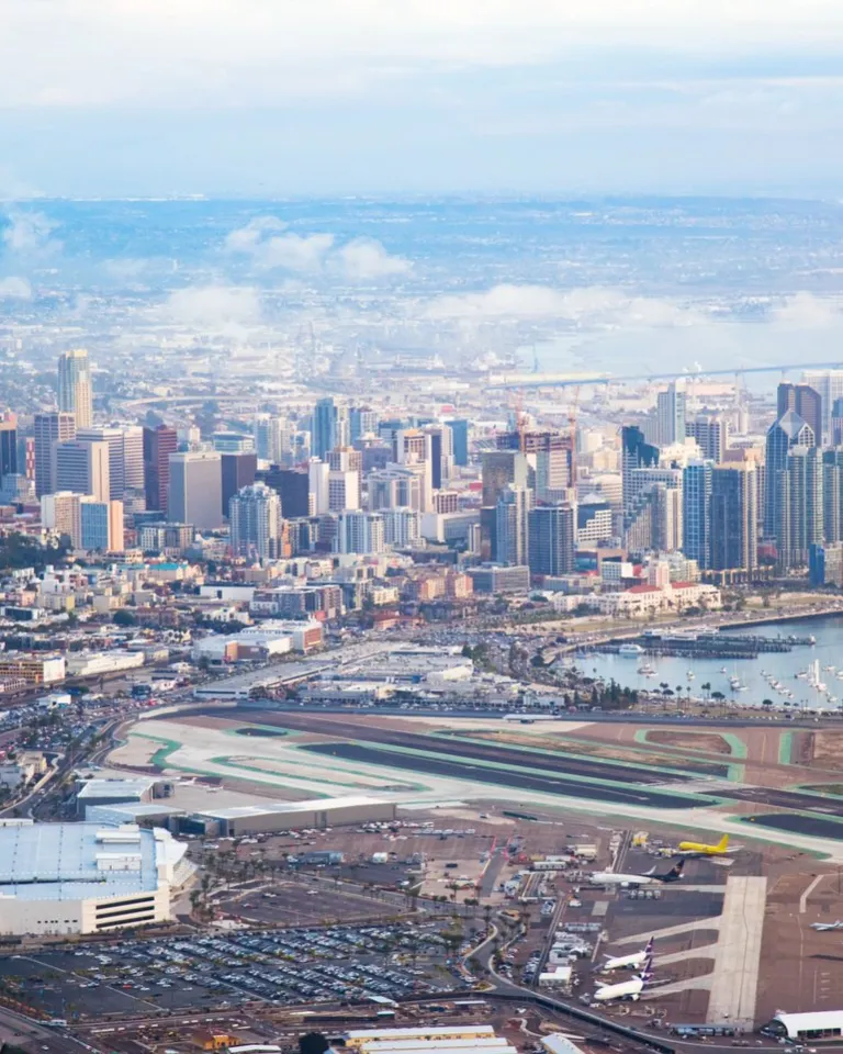 Aerial view of a city skyline with high-rise buildings, a harbor with boats, and an airport runway in the foreground.