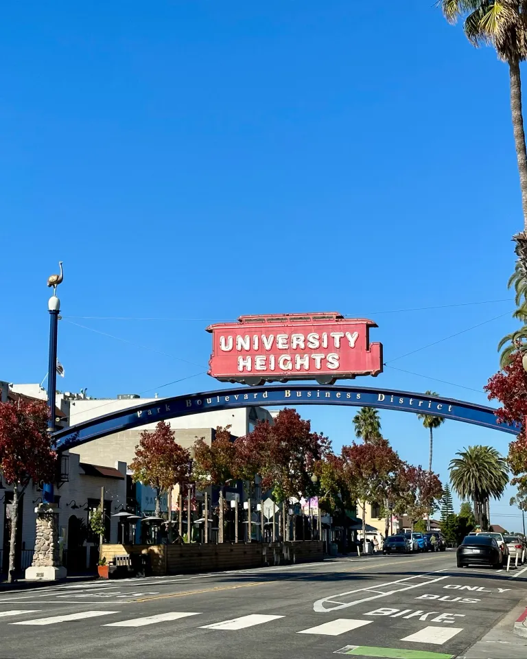 Neighborhood sign of University Heights of a red trolley overarching the main street of the neighbodhood