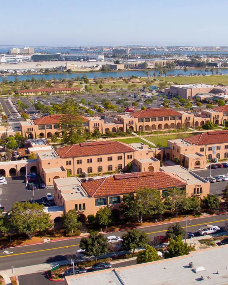 An aerial view of Liberty Station in San Diego, CA, showing red-tiled roofs, broad green lawns and blue waters under sunny skies.