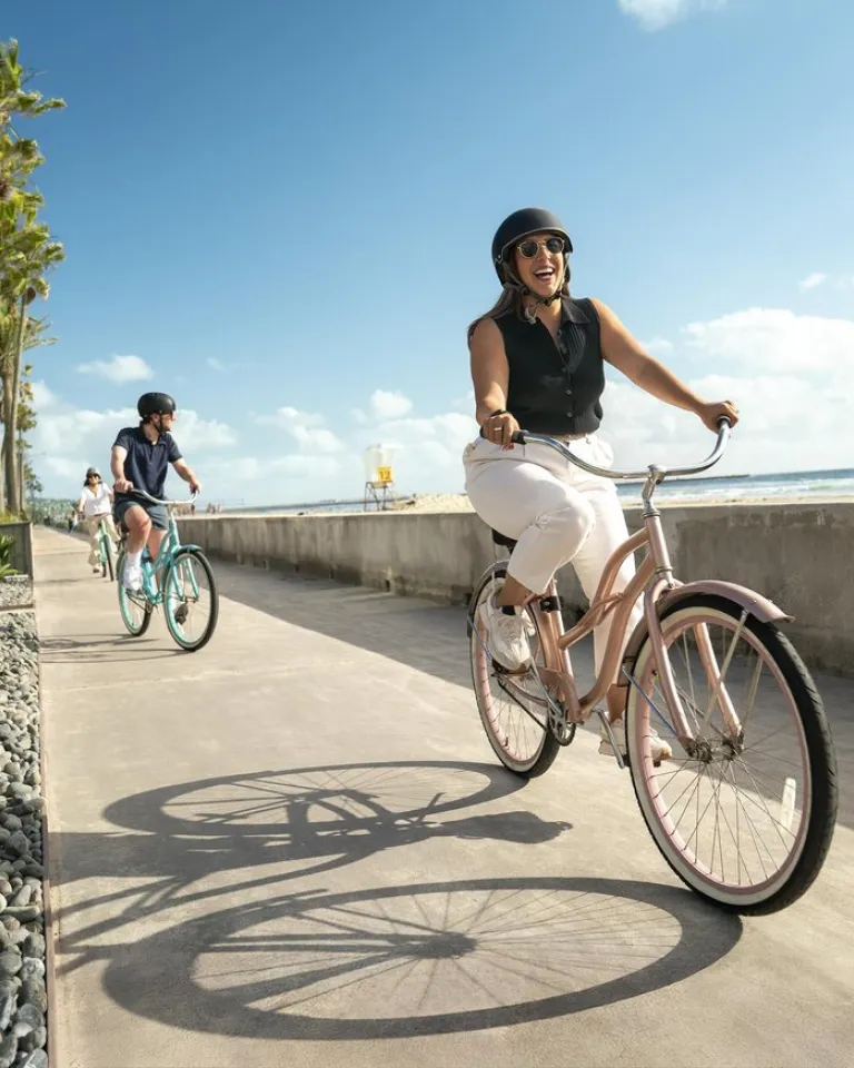 Two bicyclists ride along the Mission Beach boardwalk under sunny skies in beautiful San Diego.
