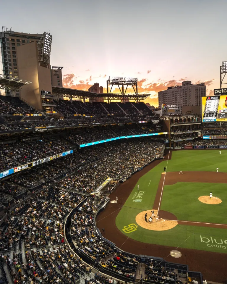 Petco Park stadium filled with Padres fans, overlooking the field at sunset with city skyline in background.