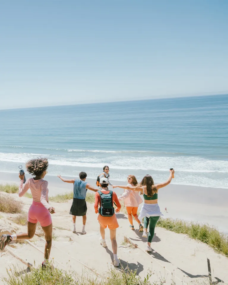 Group of friends joyfully running towards the beach under a clear blue sky.