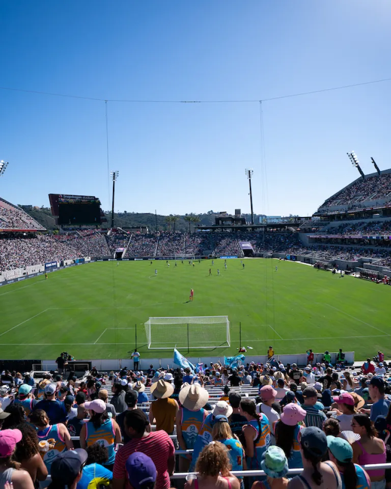 A crowded Snapdragon Stadium in San Diego on a sunny day, showing a soccer field and enthusiastic fans.