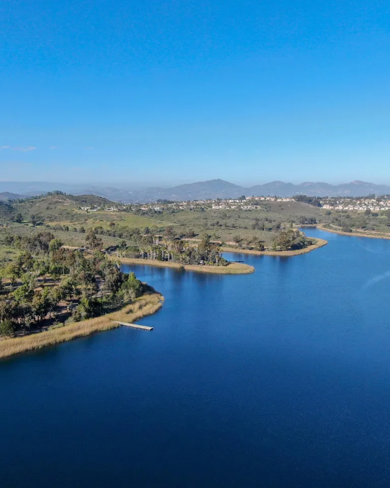 An aerial view of Lake Miramar in San Diego, showing blue waters and a green shoreline under sunny skies.
