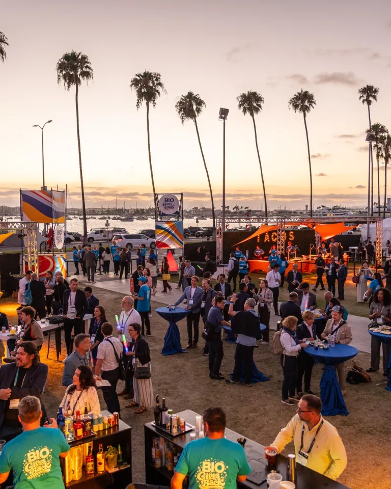 Crowd of people mingling at an outdoor event in San Diego during sunset with palm trees in the background.