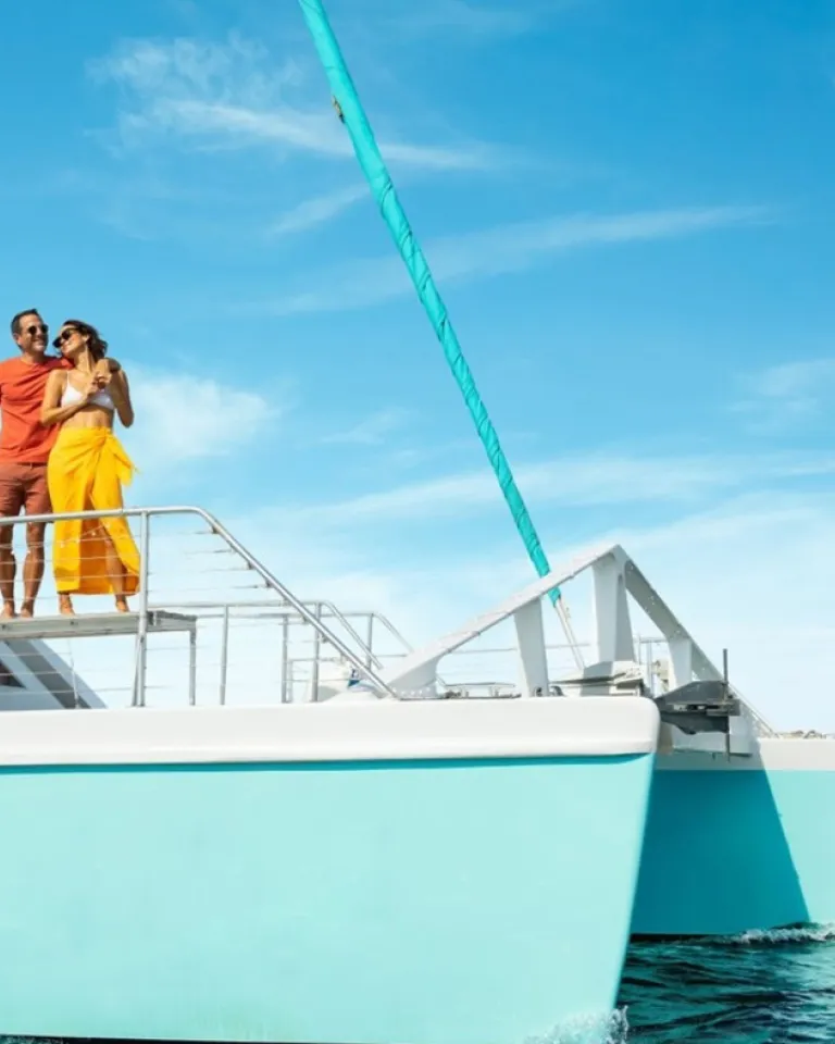 Man and woman stand on a blue sailboat with San Diego's downtown skyline in the background