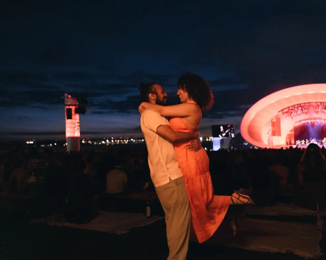 A couple dancing to the music at the Rady Shell at night with San Diego's skyline in the back ground.