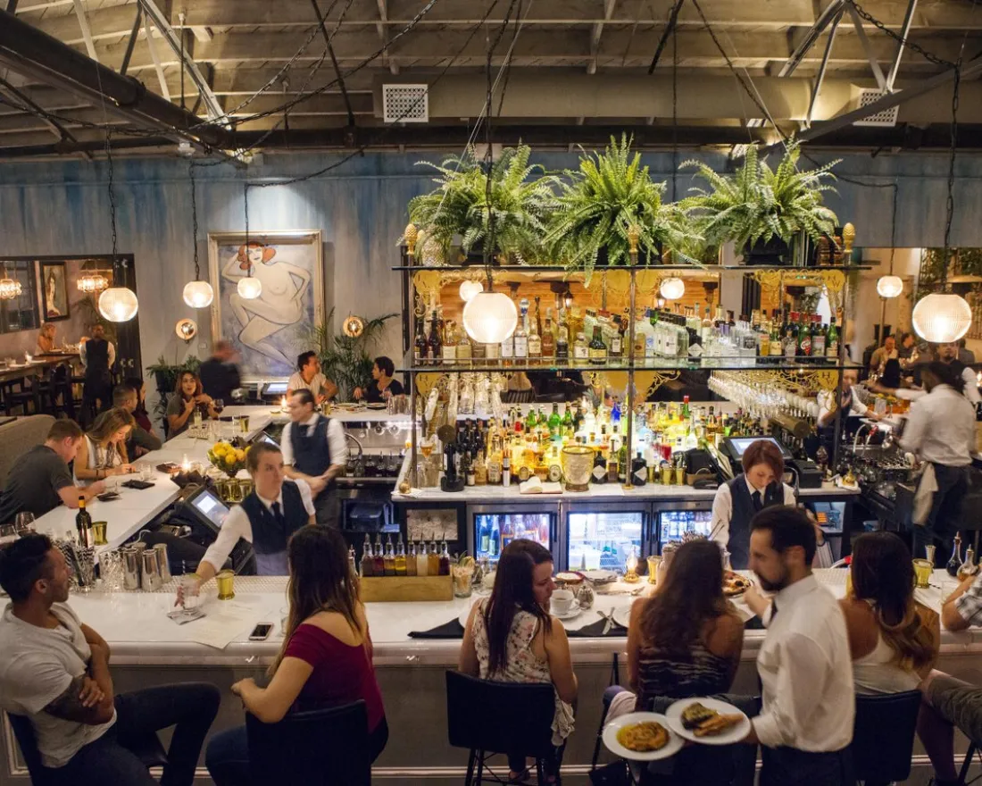 People dining at the rectangular bar of Herb & Wood in Little Italy neighborhood of San Diego, CA