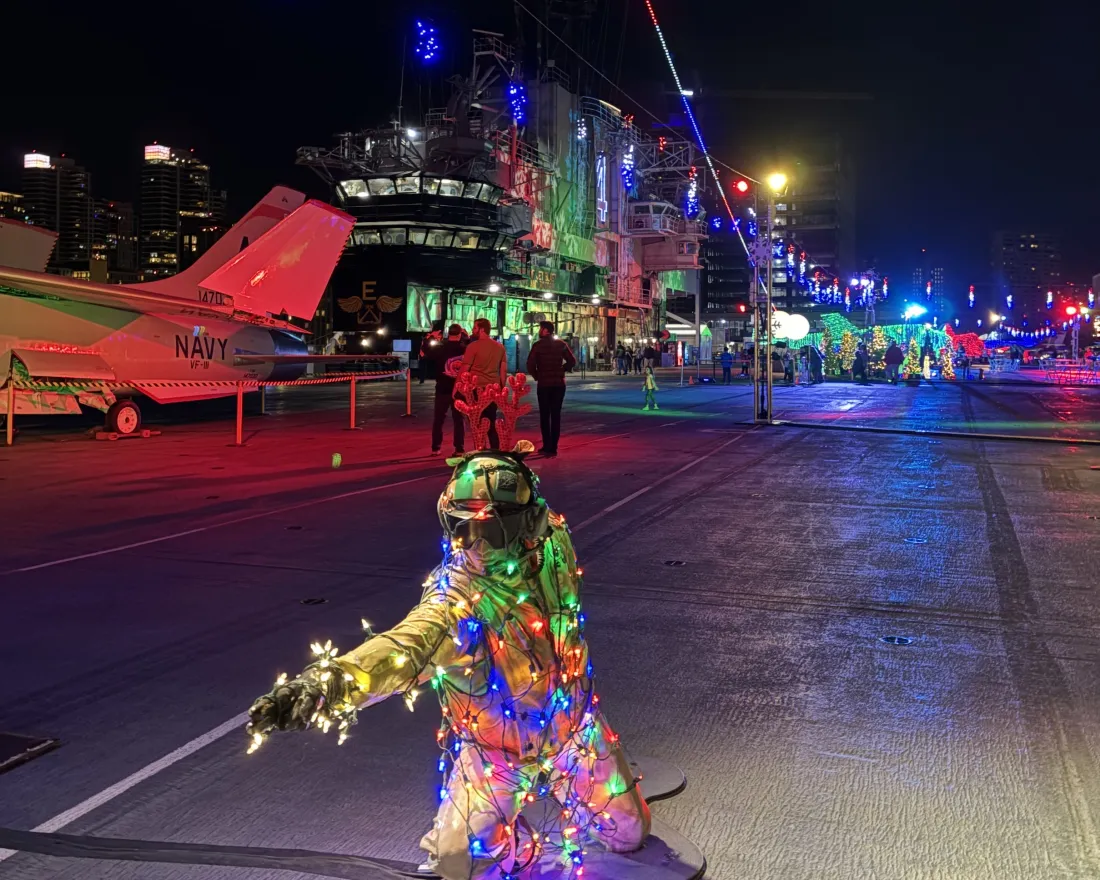 A figure draped in Christmas lights crouches on the deck of the USS Midway Museum during the Jingle Jets holiday event in beautiful San Diego.