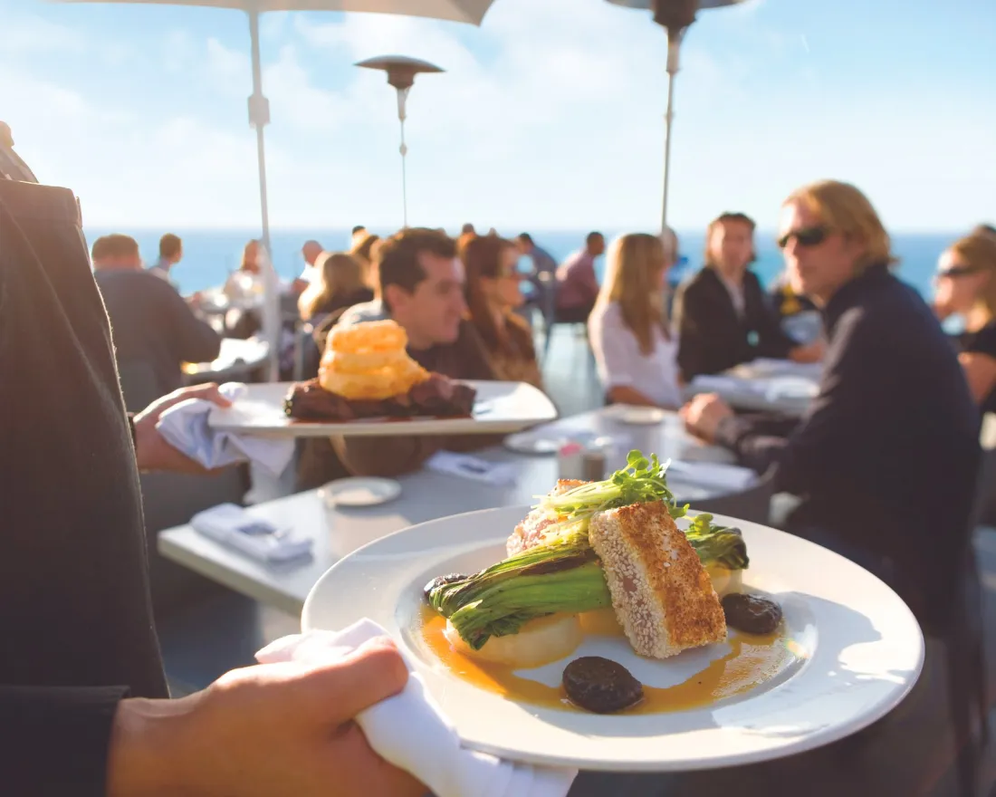 Server bring dinner plates to diners at George's at the Cove in San Diego's La Jolla