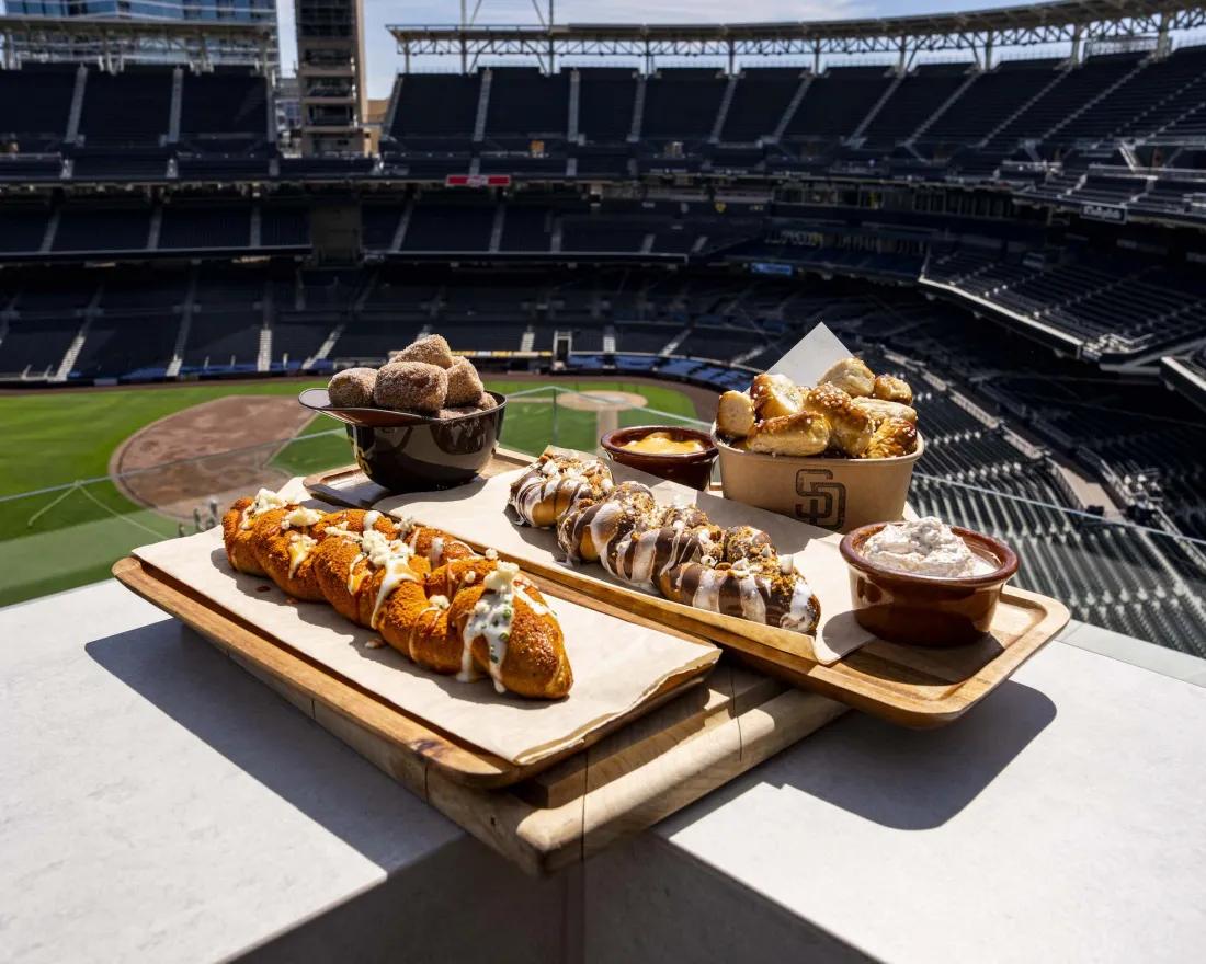 A plate of new Petco Park food offerings for 2026 is depicted against a backdrop of the San Diego ballpark.