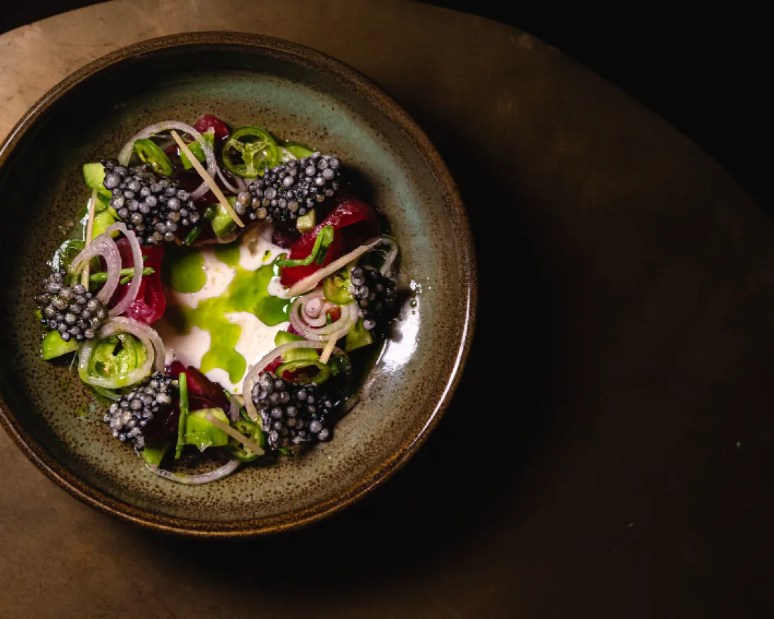 A circular plate with vibrant greens, blackberries, and thinly sliced red onions.