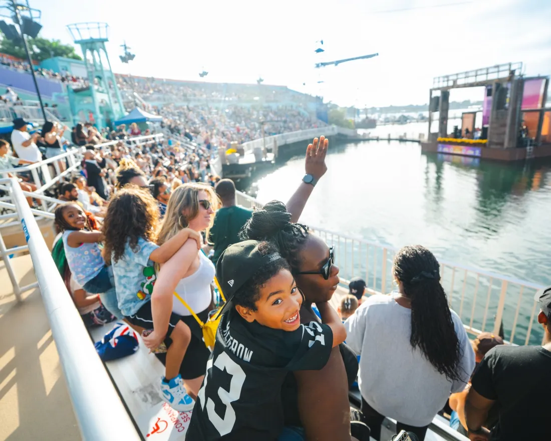 A diverse crowd watches a SeaWorld San Diego Summer Concert by the water, with excitement and smiles visible.