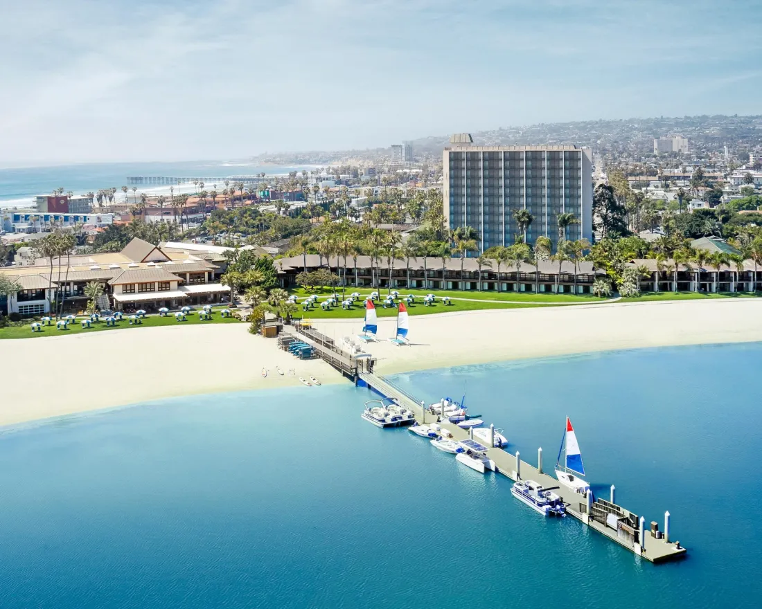 Aerial view of the Catamaran resort with a pier, surrounded by water and cityscape in the background.