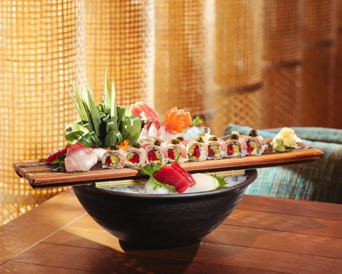 A wooden platter with assorted sushi and sashimi, decorated with fresh vegetables, on a table.