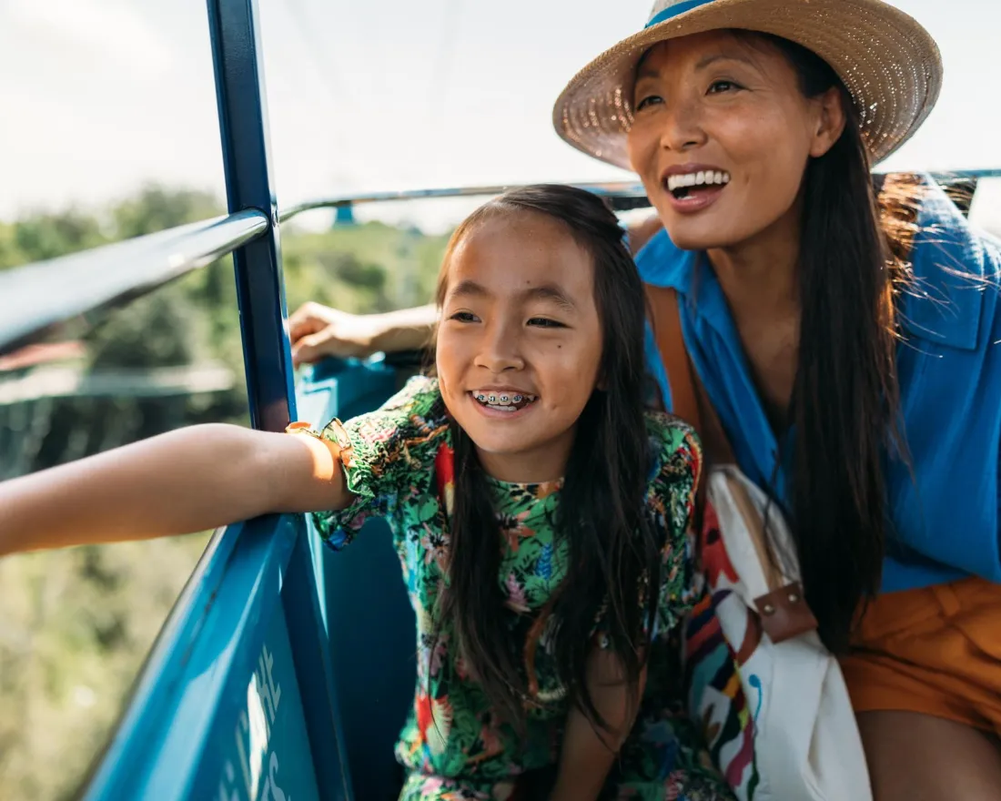 A woman and a girl smile joyfully while riding a cable car, overlooking a scenic view at the San Diego Zoo.