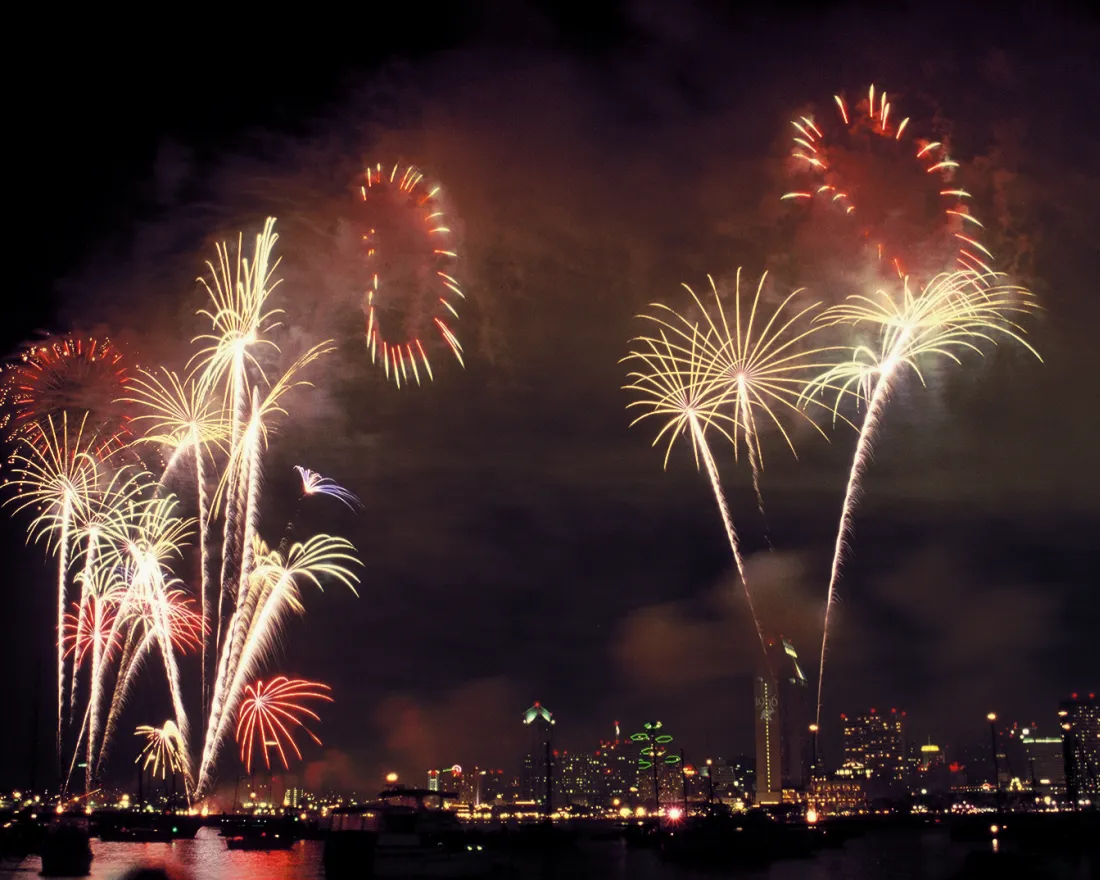 Vibrant fireworks burst over the San Diego skyline at night, reflecting in the waters of San Diego Bay.