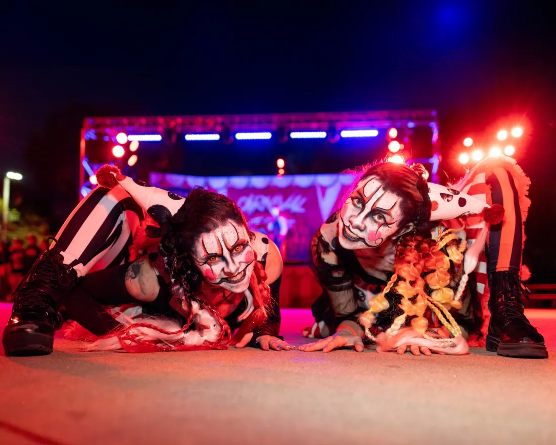 Two performers in clown-like makeup pose dramatically under colorful stage lights at SeaWorld San Diego's Howl-O-Scream halloween event.