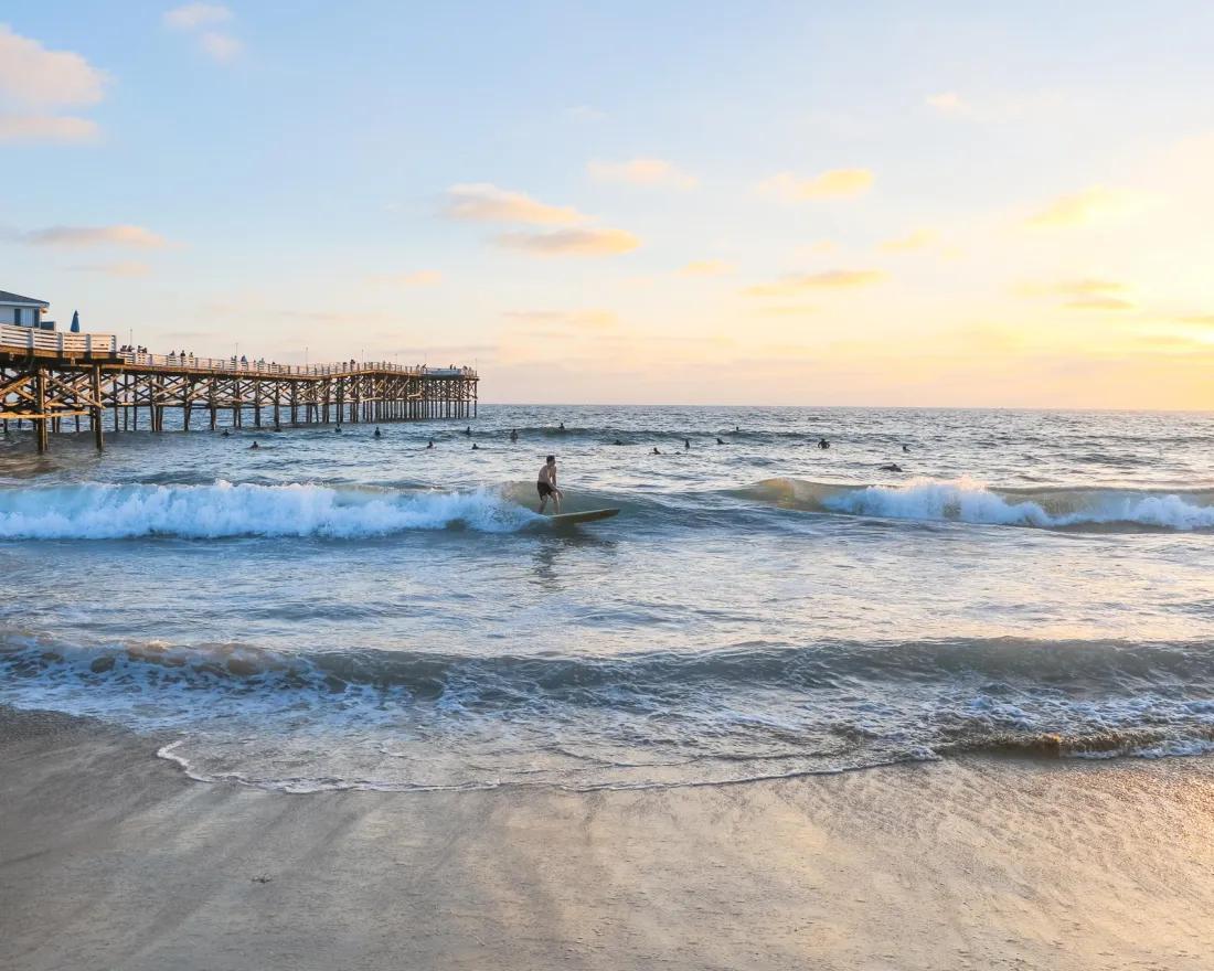 A serene beach scene at sunset with gentle waves and a person near Crystal Pier in San Diego's Pacific Beach.