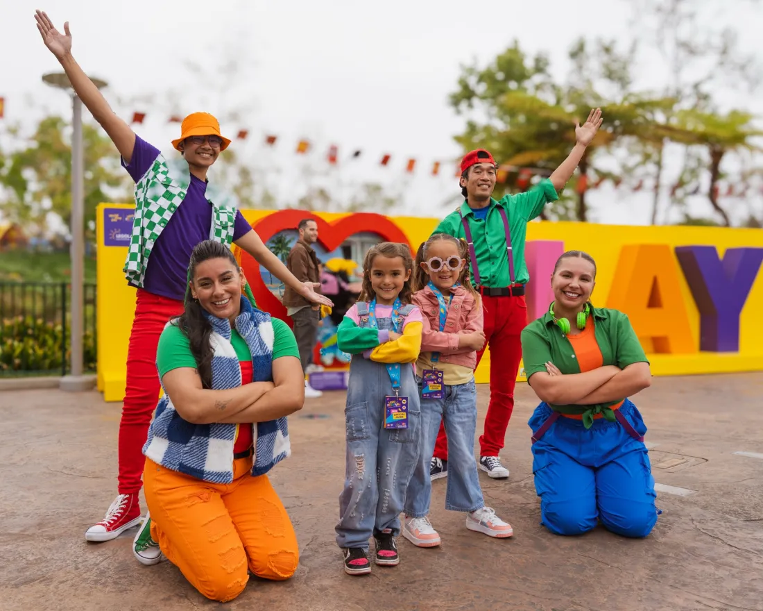 Six colorful characters posing joyfully in front of a vibrant sign at LEGOLAND California for the summer LEGO Festival.