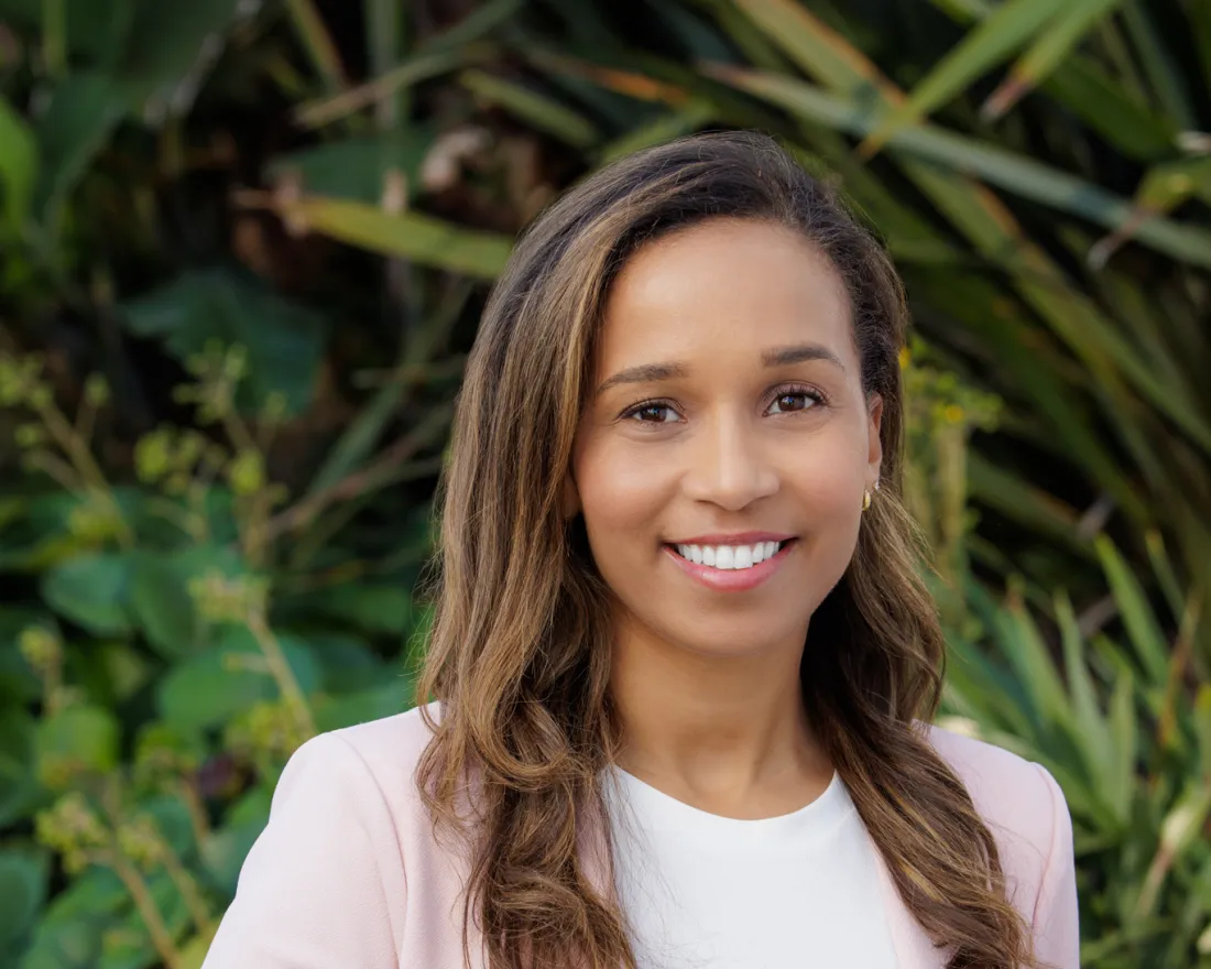 Theresa Cunningham smiling in a pink blazer, standing in front of lush green foliage.