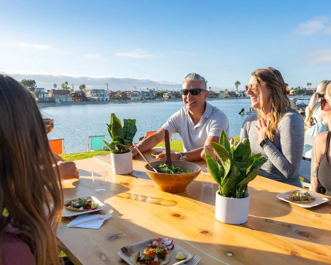 Group of friends laughing and enjoying a meal by the water on a sunny day in San Diego.